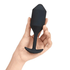 Adult hand holding black weighted silicone plug to demonstrate size and ergonomic anchor base