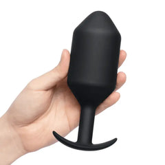 Adult hand holding black weighted silicone plug to illustrate overall size and scale