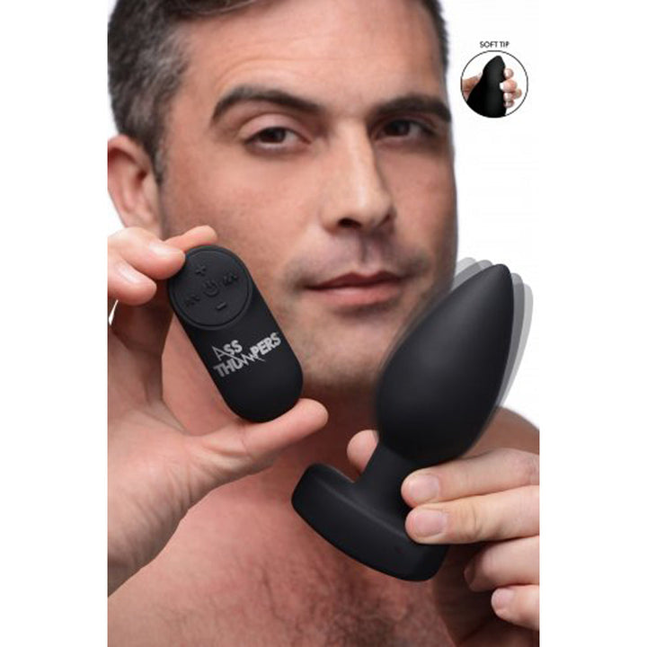 Ass Thumpers The Taper smooth black silicone anal plug held alongside its wireless remote control