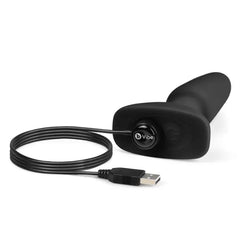 B-Vibe Rimming Plug 2 in black silicone lying flat with magnetic USB charging cable attached