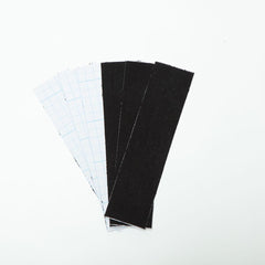 Close-up of Be Wicked adhesive breast lift tape strips fanned out, showing black fabric and peel-off backing