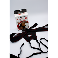 Black adjustable strap-on harness laid flat beside its Get Lucky box, showing red-stitched O-ring panel