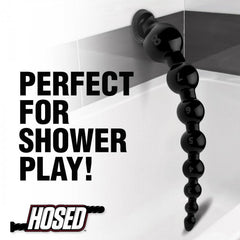 Black beaded hose attached via suction cup to shower wall, shown hanging in wet environment