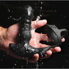 Black silicone anal plug with cock ring held under running water, showing waterproof construction