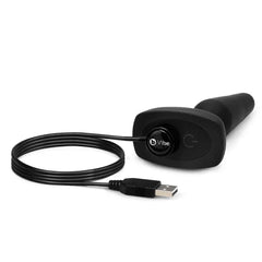 Black silicone anal plug lying beside its magnetic USB charging cable on white background