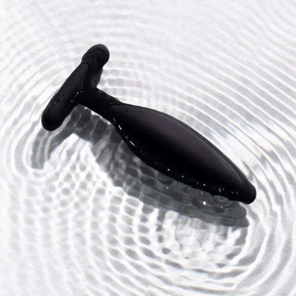 Black silicone butt plug lying on rippling water surface, highlighting waterproof design
