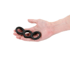 Black silicone triple cock ring held in an open palm, showing compact wearable size