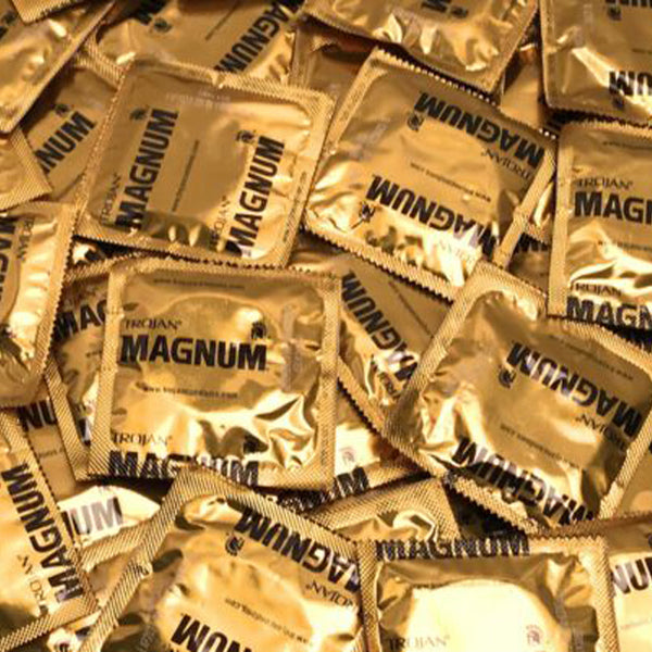 Bulk quantity of Trojan Magnum gold foil condom wrappers arranged together, filling the frame