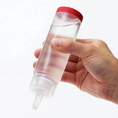 Clear squeeze bottle with red cap held in hand, showing transparent water-based formula inside