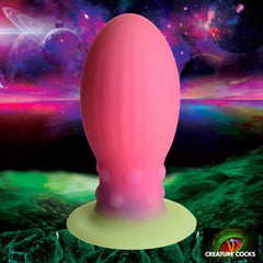 Creature Cocks Xeno Egg glow-in-the-dark silicone plug, pink with green luminous base, space backdrop