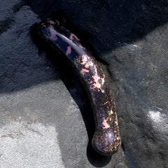 Curved rhodonite crystal dildo resting on natural stone surface, showing textured detail