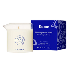 Dame Massage Oil Candle beside bold blue box showing Green Tea, Fig and Cedarwood scent