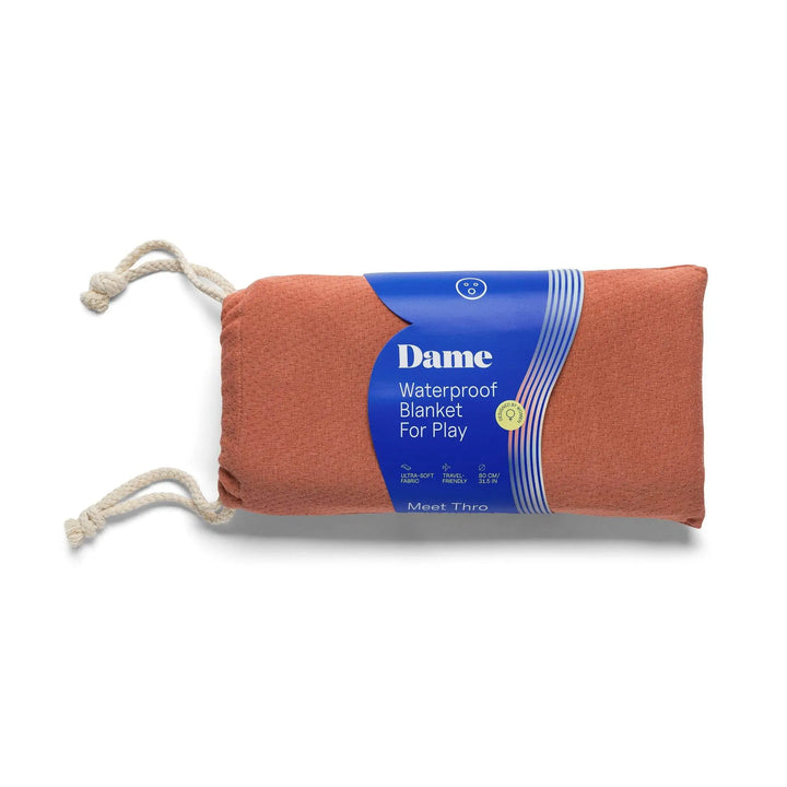 Dame Thro waterproof blanket rolled in terra cotta, bundled with rope ties for travel