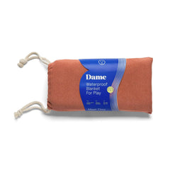 Dame Thro waterproof blanket rolled in terra cotta, bundled with rope ties for travel
