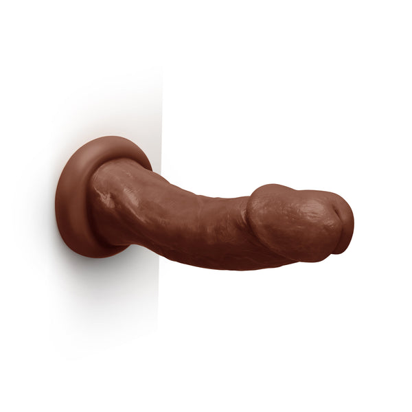 Dark brown realistic dildo mounted on white wall via suction base, shown horizontally for scale