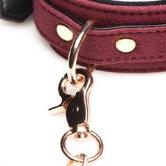 Detail of gold-tone lobster clasp and D-ring connector on burgundy velvet bondage collar