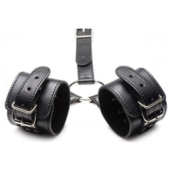Close-up of dual wrist cuffs connected by O-ring, featuring silver buckles and stitched edging