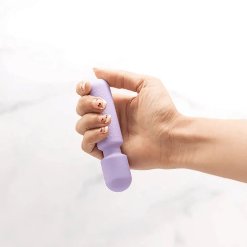 Hand holding the Emojibator Tiny Wand Vibrator in soft lavender silicone against marble