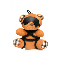 Front view of brown plush bound teddy bear keychain with plaid ears and faux-leather blindfold