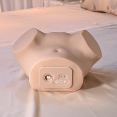 Front-on view of the stroker upright on bedding clearly showing the belly-side control panel and charging port