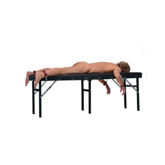 Full side view of person lying prone on black bondage massage bed with wrist and ankle cuffs