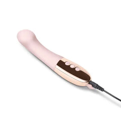 Gee vibrator lying flat with USB charging cable attached to rose gold base