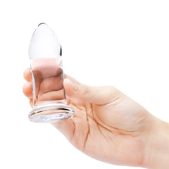 Hand cradling medium clear glass anal dilator, showing bulbous body and ridged flat base