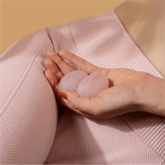 Hand cradling two smooth oval rose quartz yoni eggs against soft pink ribbed fabric