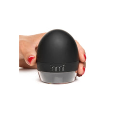 Hand gripping the closed black egg-shaped Inmi Lady Licker with matte silicone exterior and branded base