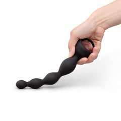 Hand gripping finger loop of black silicone anal beads horizontally, showing flexible strand
