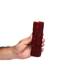 Hand gripping lit red Thorn Drip Candle upright, showing scale and textured wax exterior