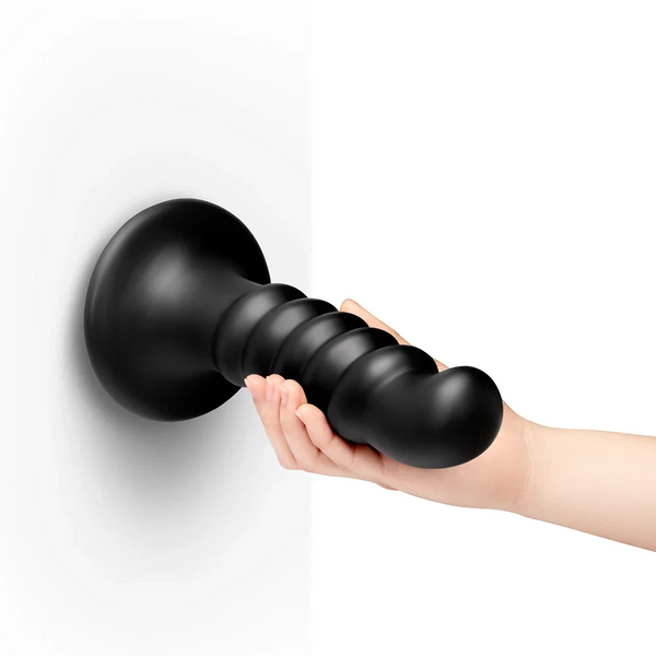 Hand gripping mounted b-Vibe Krush ribbed dildo on wall, showing true 9.5-inch scale