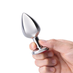 Hand gripping a polished silver metal butt plug showing tapered tip and narrow neck