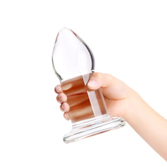 Hand gripping the smooth cylindrical shaft of the clear glass anal dilator from the side