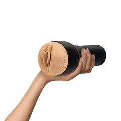 Hand gripping the stroker horizontally displaying the skin-tone vaginal opening end toward camera