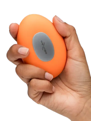 Hand gripping We-Vibe Temp tangerine vibrator showing palm-friendly oval size and silver logo panel