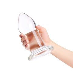 Hand holding the b-Vibe glass anal dilator tilted to show its tapered tip and wide base