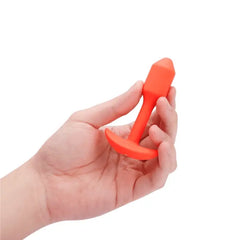 Hand holding b-Vibe Snug Plug 1 to show compact size of the coral silicone anal plug