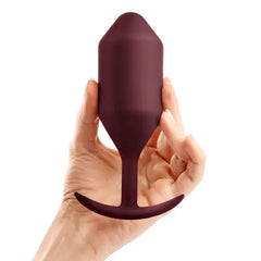 Hand holding b-Vibe Snug Plug 5 dark red weighted silicone plug to illustrate product scale