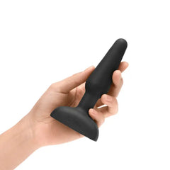Hand holding black silicone anal plug upright to show compact size and tapered tip