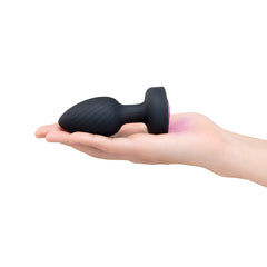 Hand holding black silicone butt plug with pink LED base lit to show compact size
