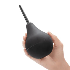 Hand holding black silicone enema bulb to show palm-sized scale and squeeze grip