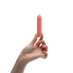 Hand holding The Bullet vibrator upright showing single control button on coral silicone body