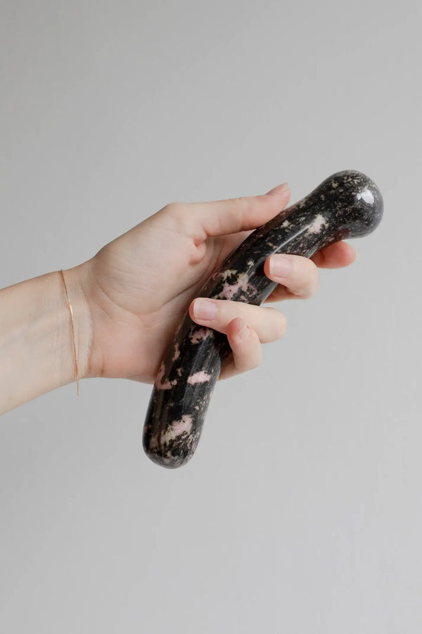 Hand holding the Chakrubs rhodonite dildo, showing curved dual-end shape and polished size