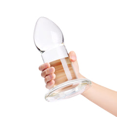 Hand holding the clear glass anal dilator, showing its large cylindrical shaft and wide base