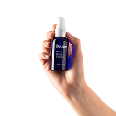 Hand holding Dame Essential Aloe Lube 2 oz pump bottle to show compact portable size