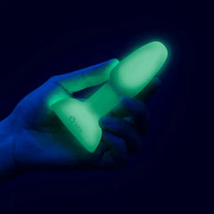 Hand holding large glow-in-the-dark silicone anal plug showing its tapered shape and base