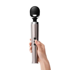 Hand holding Le Wand Die Cast Massager upright, finger pressing control buttons on handle