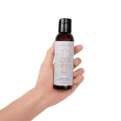 Hand holding Le Wand Natural Intimate Lubricant 118ml bottle, showing compact travel-friendly size