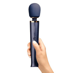 Hand holding Le Wand Petite navy massager upright, showing ergonomic handle grip and button placement